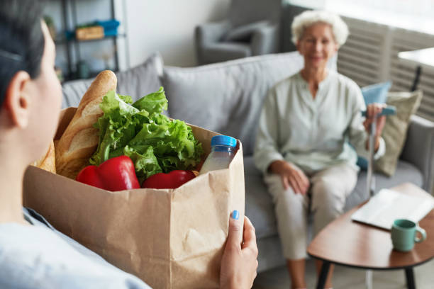 Portrait of female caregiver bringing groceries to senior woman, copy space